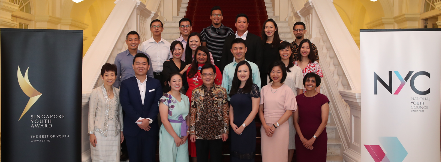 Group portrait on stairs with "Singapore Youth Award" and "NYC National Youth Council Singapore" banners.